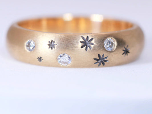 A rounded yellow gold ring band with hand carved, black stars sprinkled between 3 bright white full cut diamonds that are flush set into the gold.