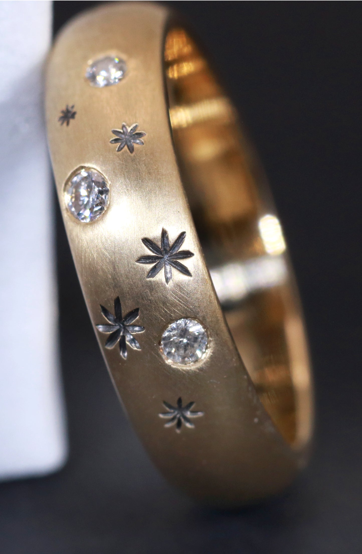A rounded yellow gold ring band with hand carved, black stars sprinkled between 3 bright white full cut diamonds that are flush set into the gold.