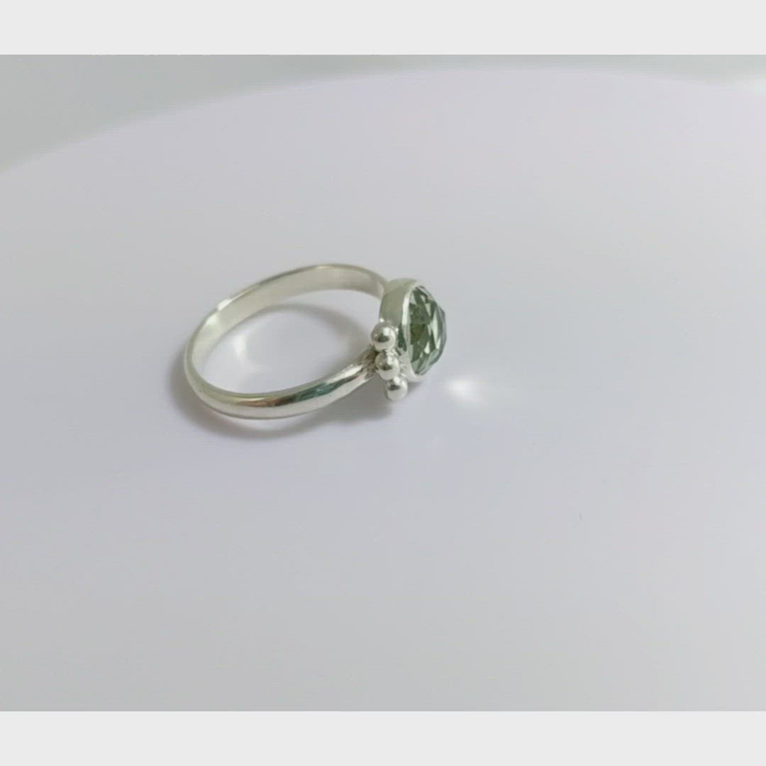 A video of a silver ring with an 8mm round rose cut green amethyst gemstone set in sterling silver. 3 Silver bubble accents aligned along the side.