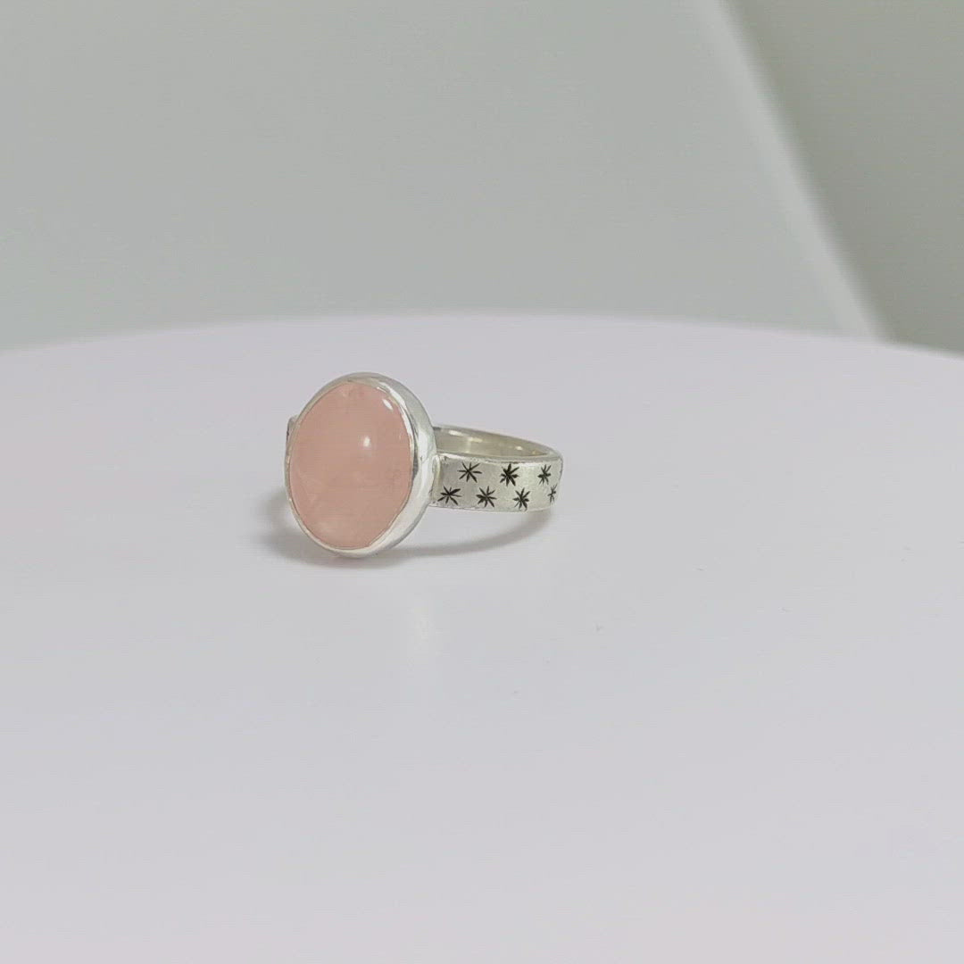 Oval natural gemstone set in sterling silver bezel on a wide sterling silver ring band with checker board of hand cut black stars on either side.