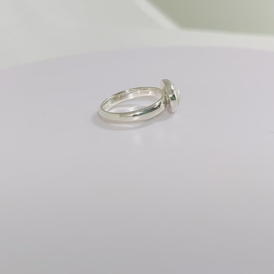 Oval natural white opal set in sterling silver bezel on a sterling silver ring band.