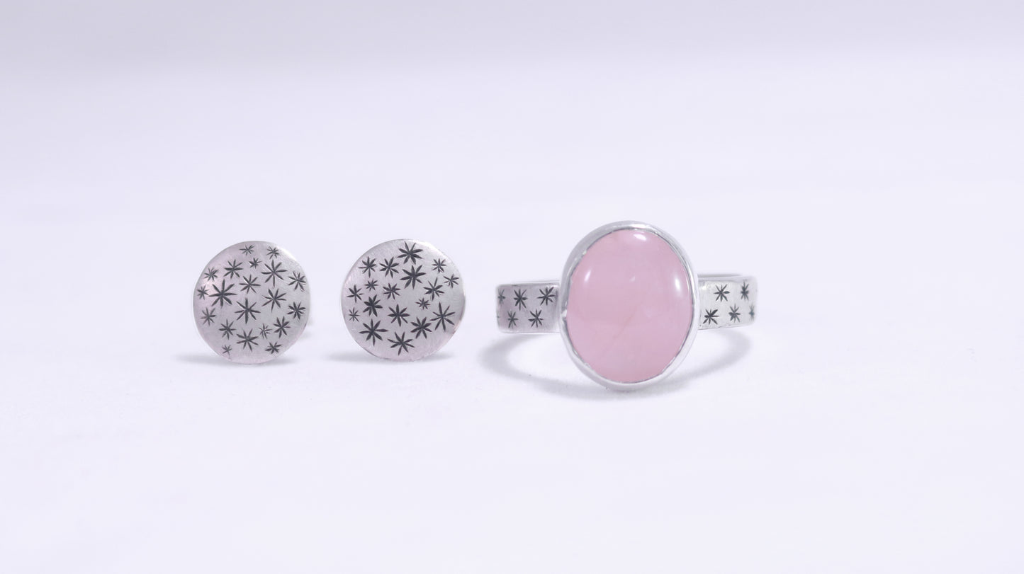 Oval natural gemstone set in sterling silver bezel on a wide sterling silver ring band with checker board of hand cut black stars on either side.