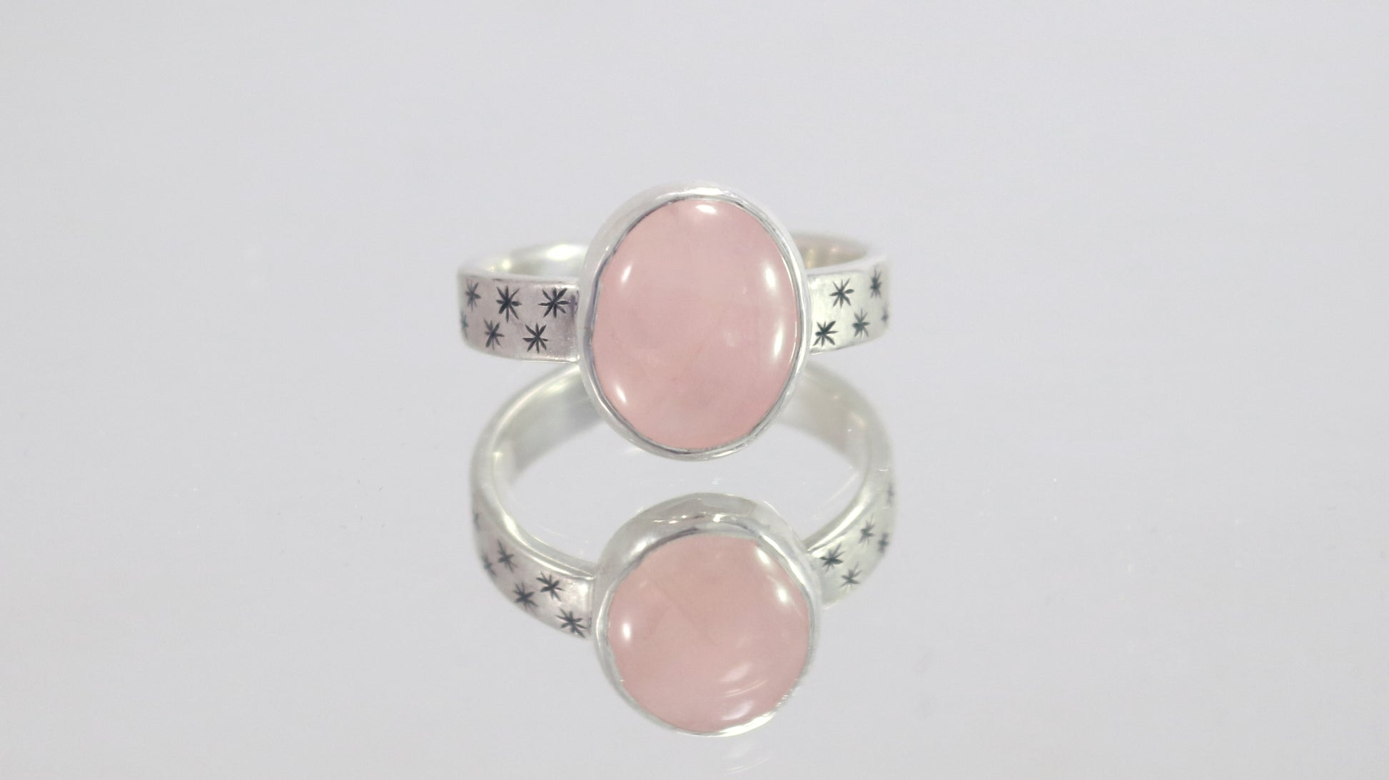 Oval natural gemstone set in sterling silver bezel on a wide sterling silver ring band with checker board of hand cut black stars on either side.