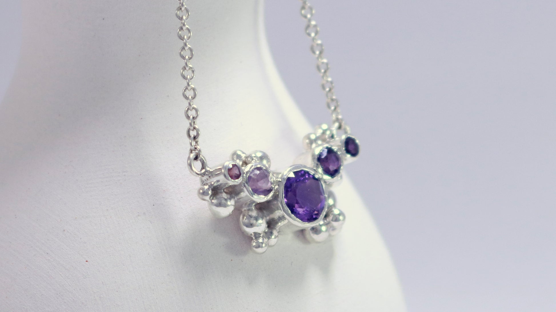 Different shades of round amethyst stones, surrounded by silver bubbles on a silver chain.