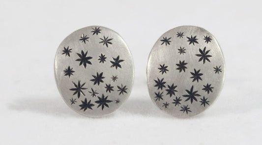 A pair of domed oval sterling silver studs covered in hand carved, black stars.