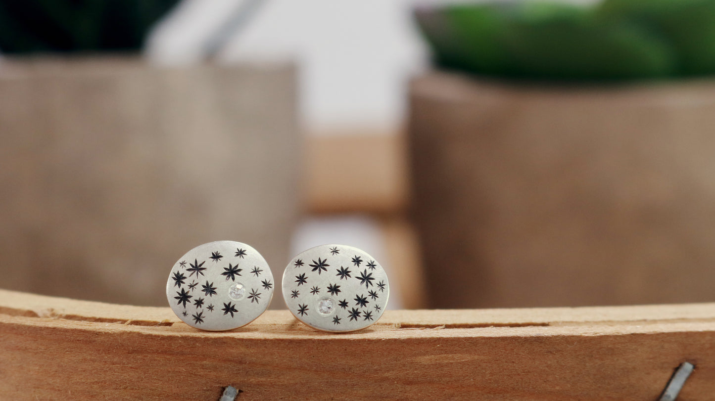 A pair of domed oval sterling silver studs covered in hand carved, black stars and one white diamond..