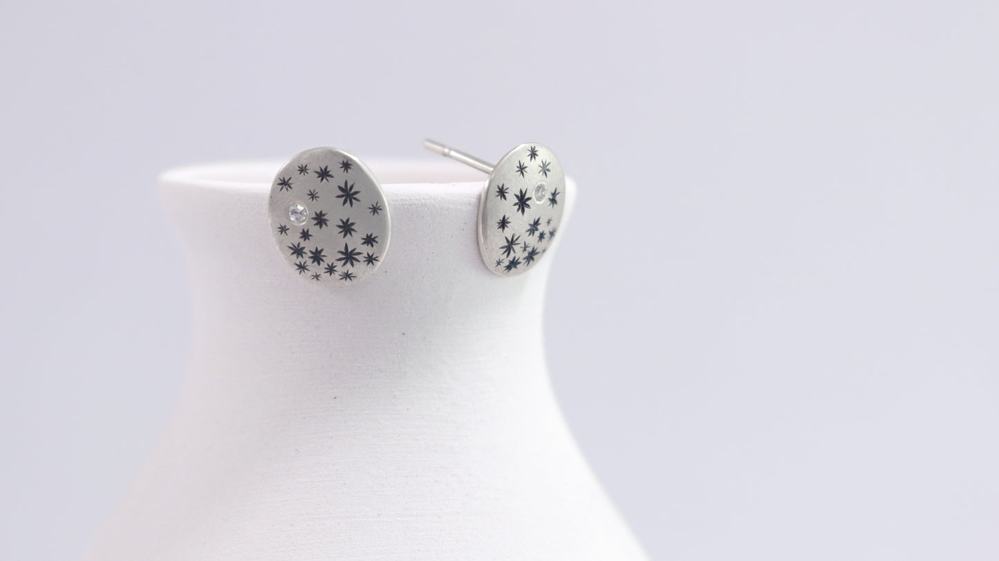 A pair of domed oval sterling silver studs covered in hand carved, black stars and one white diamond..