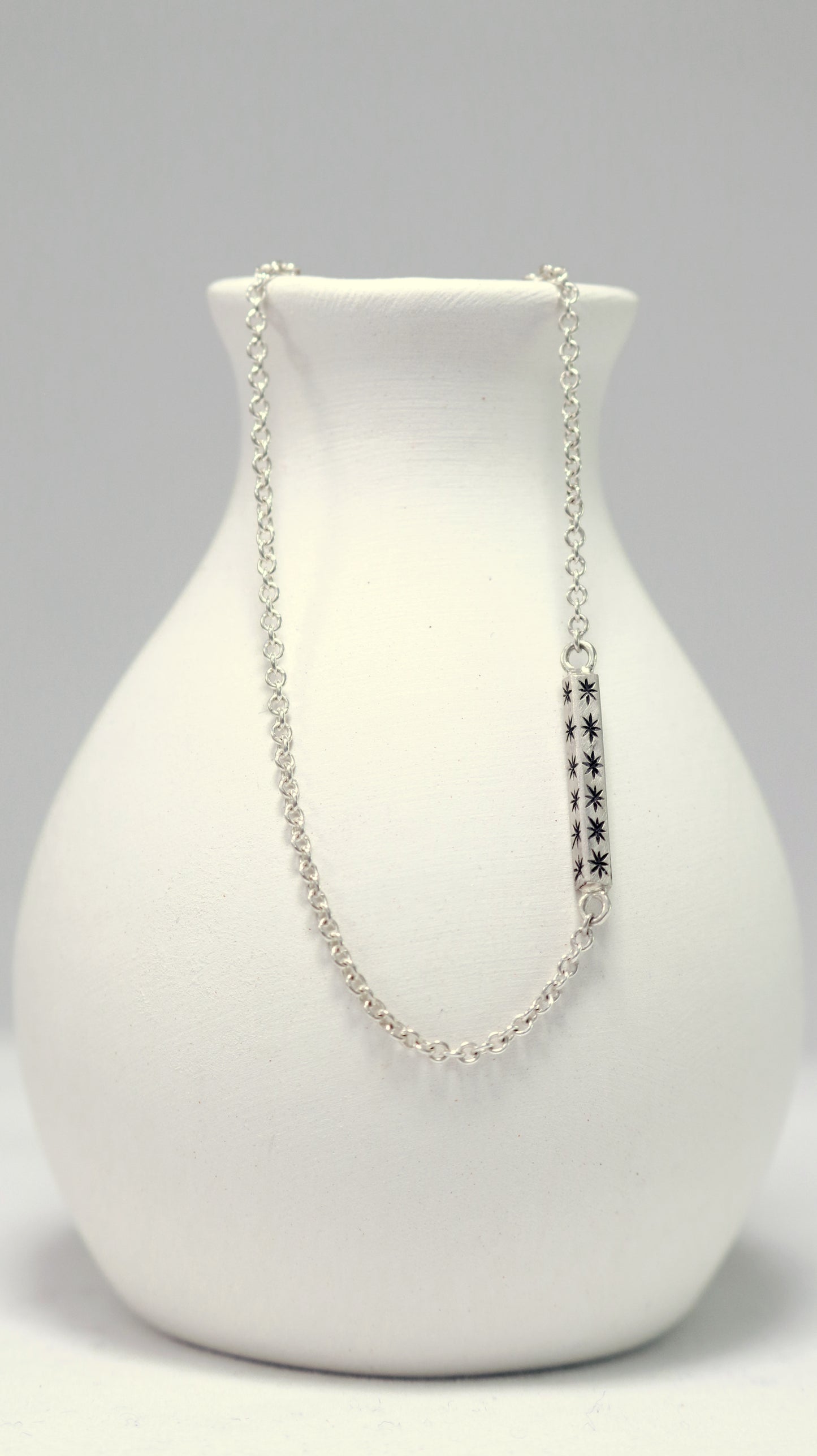 Sterling silver bar necklace with hand cut black stars on every side on a sterling silver chain.