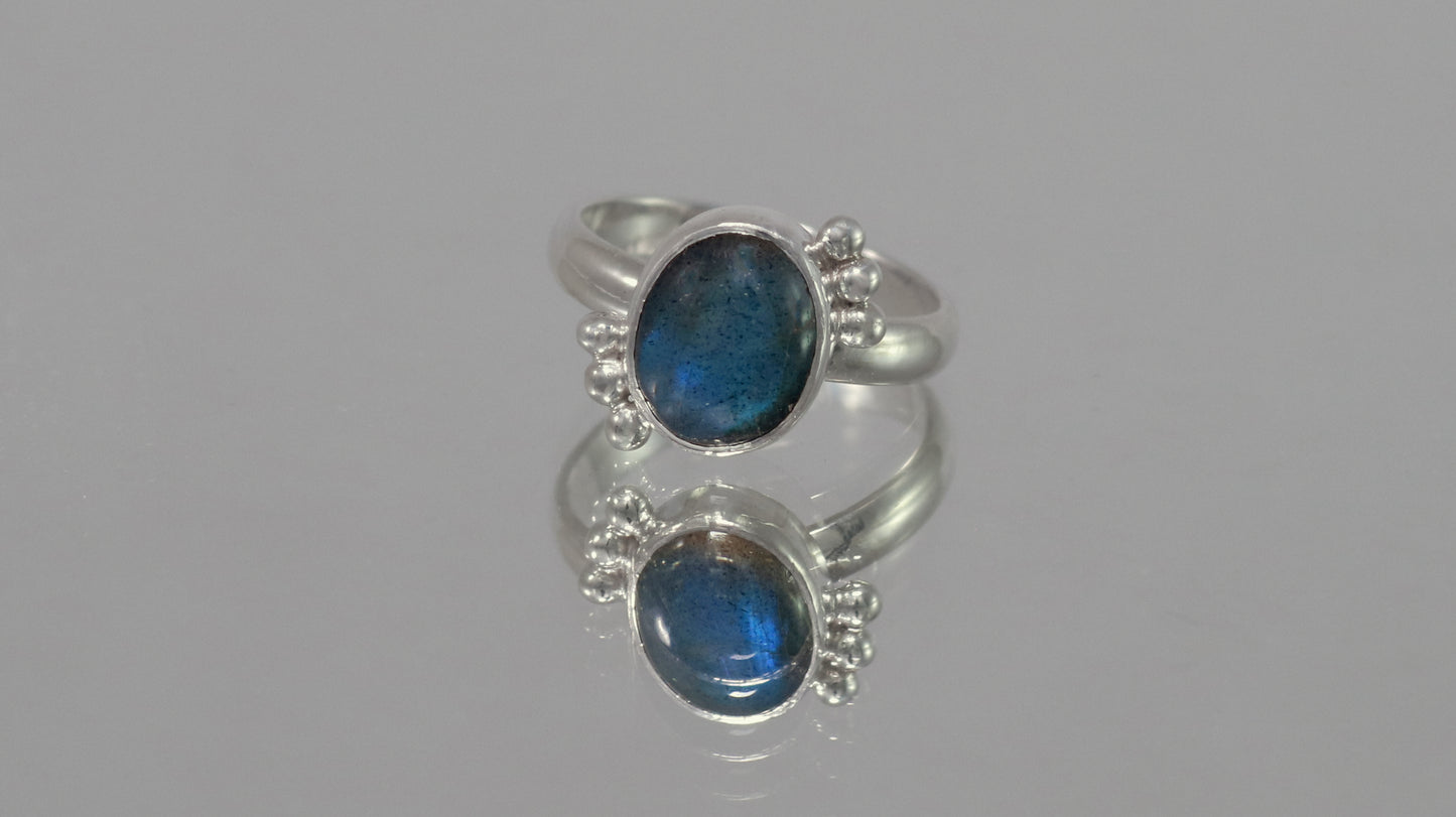 A royal blue, oval labradorite stone is bezel set on a sterling silver ring. On opposite diagonals are three silver bubbles with a total of 6 bubbles on the stone.