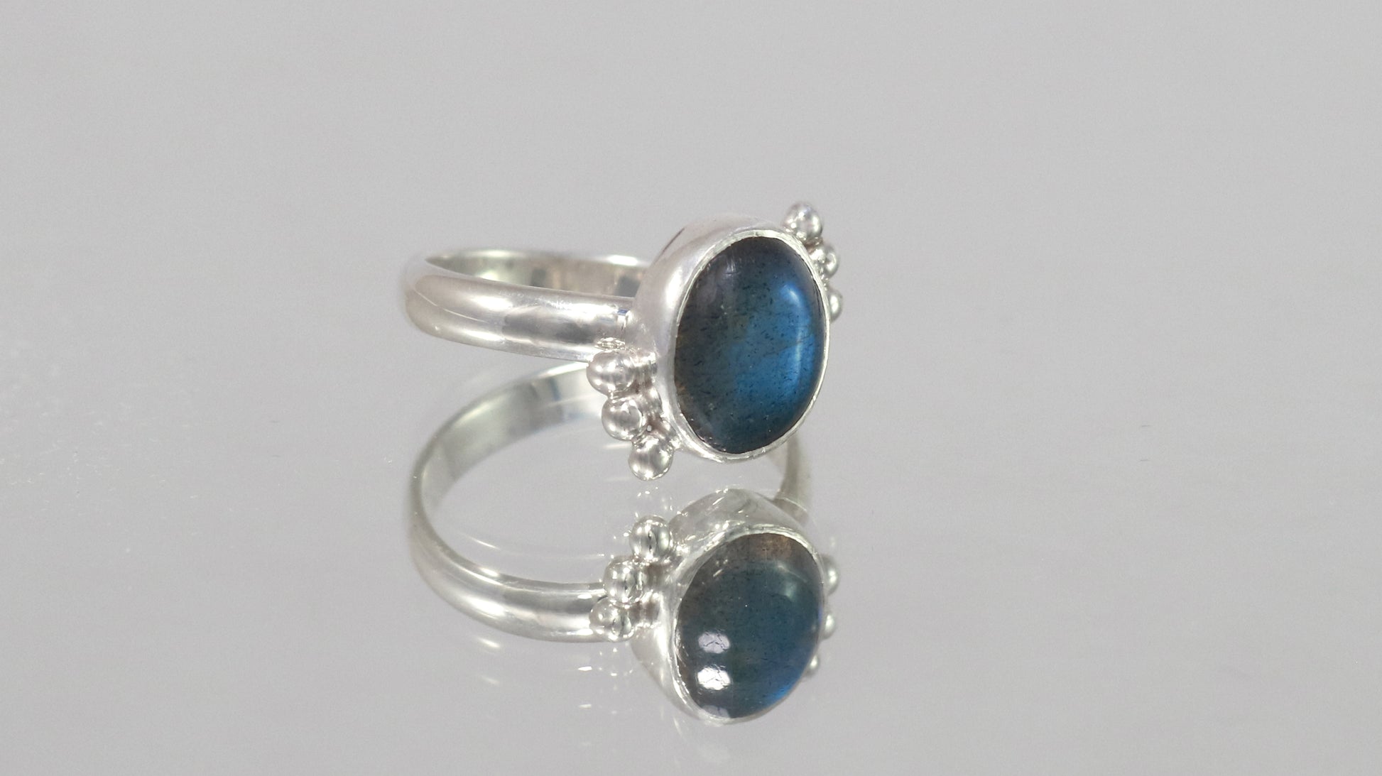 A royal blue, oval labradorite stone is bezel set on a sterling silver ring. On opposite diagonals are three silver bubbles with a total of 6 bubbles on the stone.