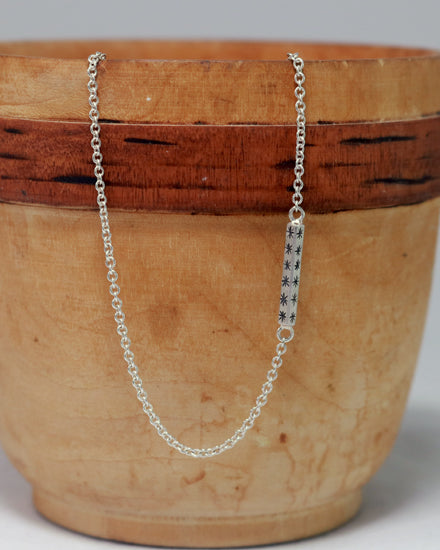 Sterling silver bar necklace with hand cut black stars on every side on a sterling silver chain.