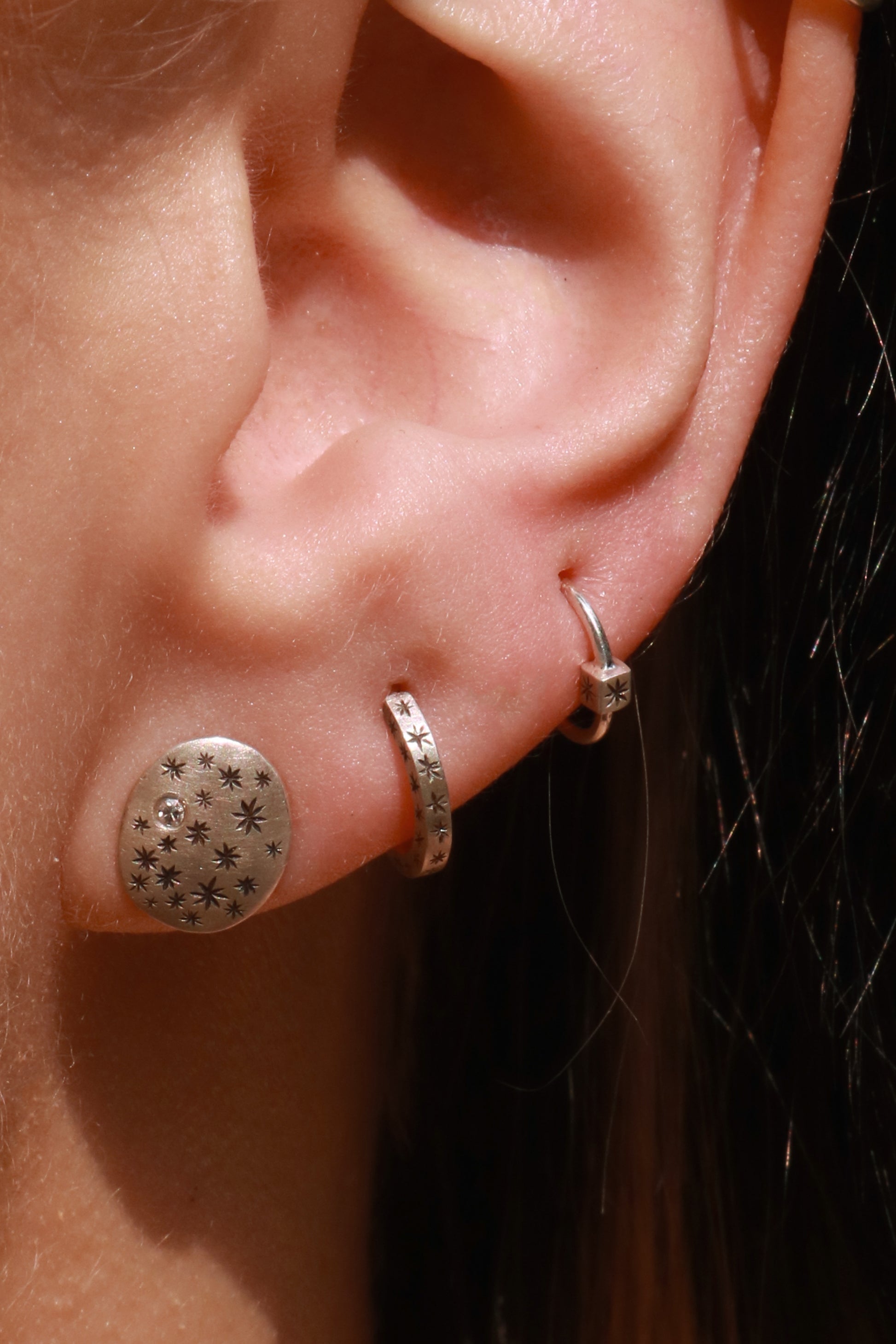 A model wearing hoops made from 1.5mm x 1.5mm square sterling silver, hand cut black stars on all outward facing sides.