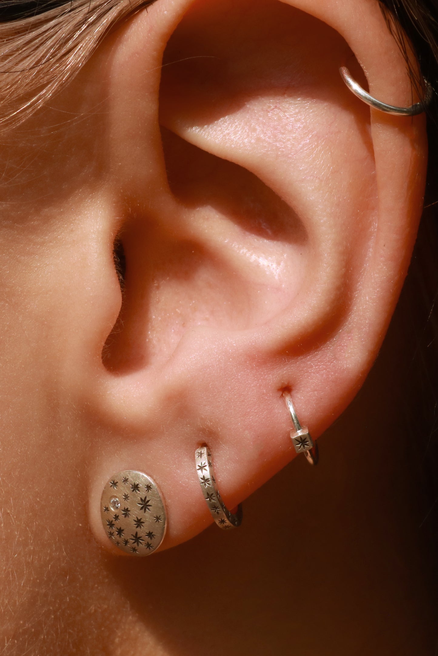 A model wearing hoops made from 1.5mm x 1.5mm square sterling silver, hand cut black stars on all outward facing sides.