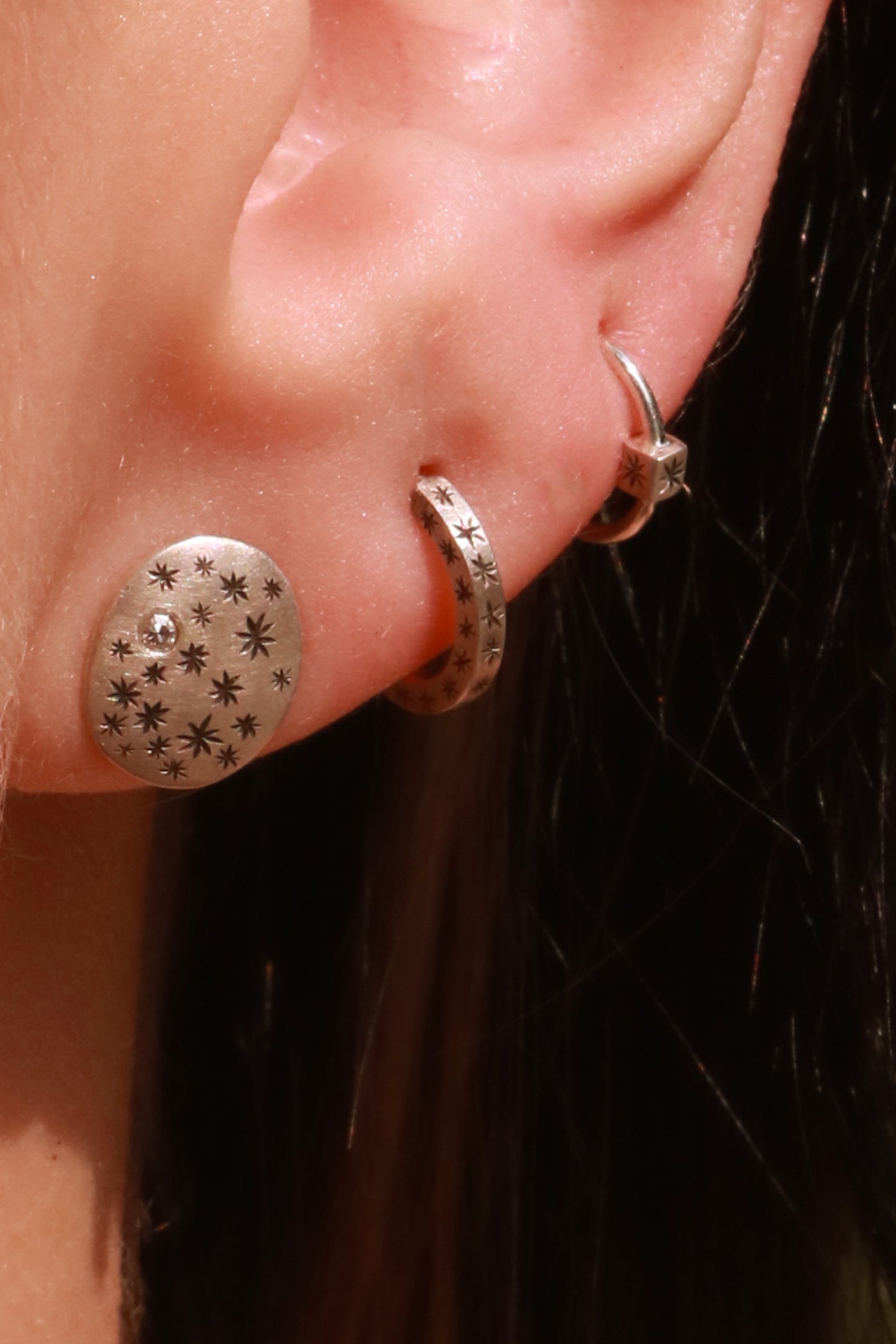 A pair of domed oval sterling silver studs covered in hand carved, black stars and one white diamond..