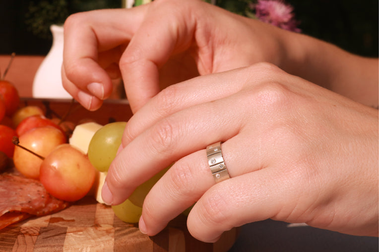 A model wearing a thick silver ring band with randomly spaced black line details is flush set with 5 various sized diamonds.