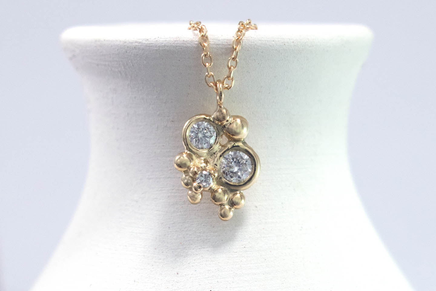 Three diamonds, decreasing in size, set in 14k yellow gold bezels, surrounded by randomly placed gold bubbles. on a 14k yellow gold chain.