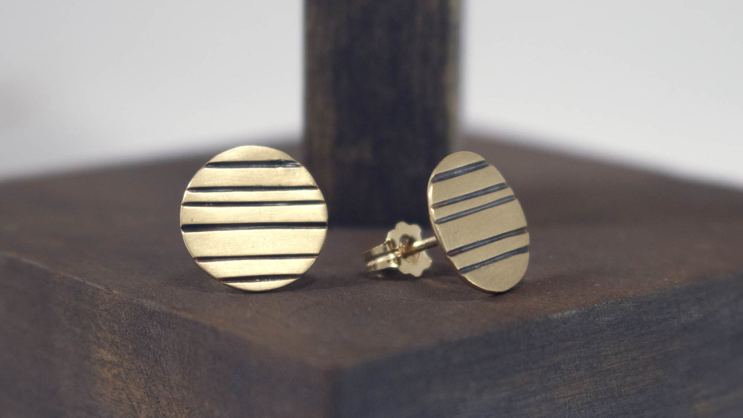 Round 14k gold disc studs with black lines randomly spaced.