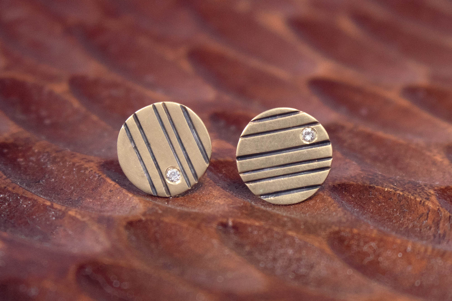 Round 14k gold disc studs with black lines randomly spaced and a single white diamond flush set at the edge.