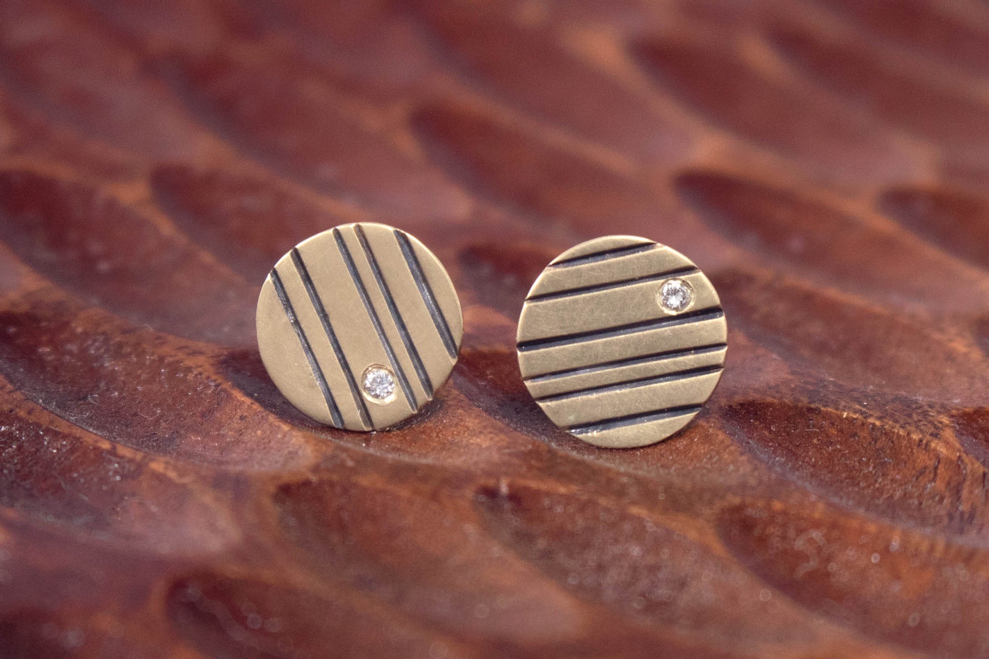Round 14k gold disc studs with black lines randomly spaced and a single white diamond flush set at the edge.