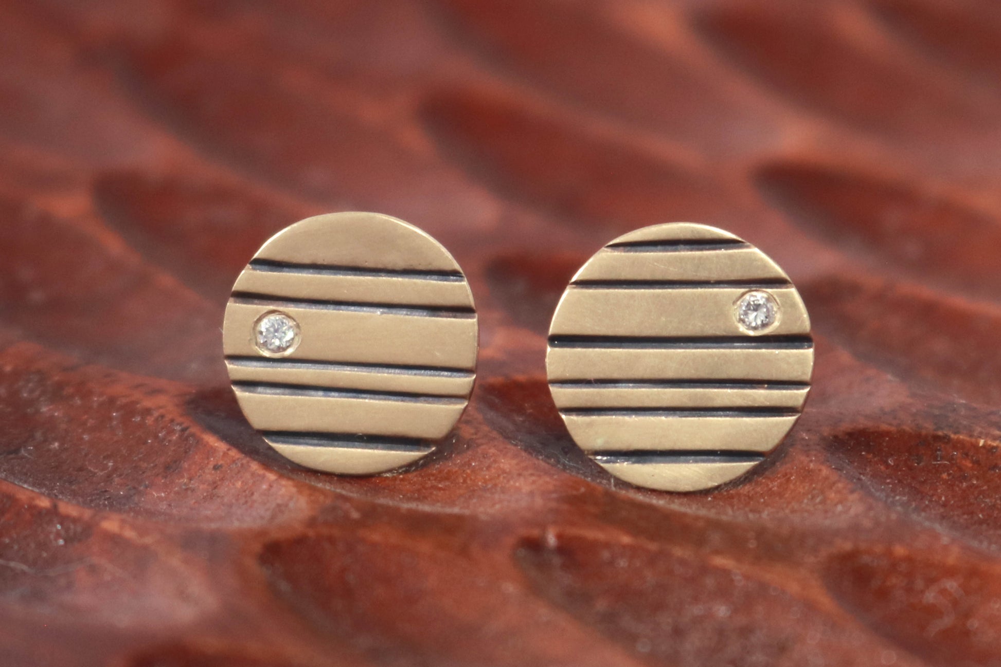 Round 14k gold disc studs with black lines randomly spaced and a single white diamond flush set at the edge.