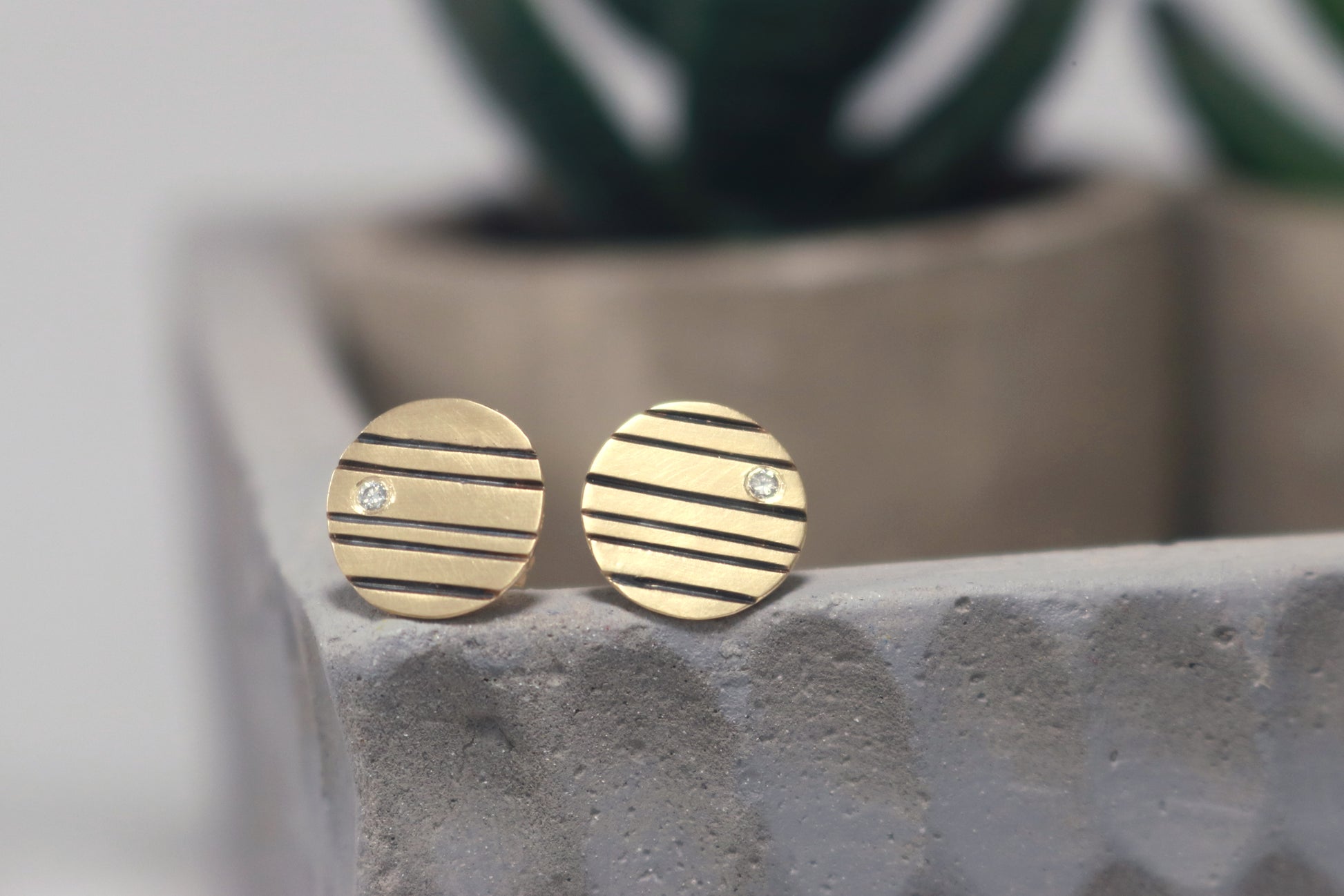Round 14k gold disc studs with black lines randomly spaced and a single white diamond flush set at the edge.
