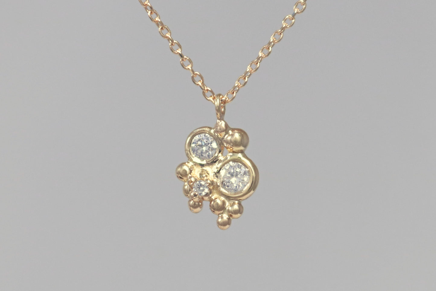 Three diamonds, decreasing in size, set in 14k yellow gold bezels, surrounded by randomly placed gold bubbles. on a 14k yellow gold chain.