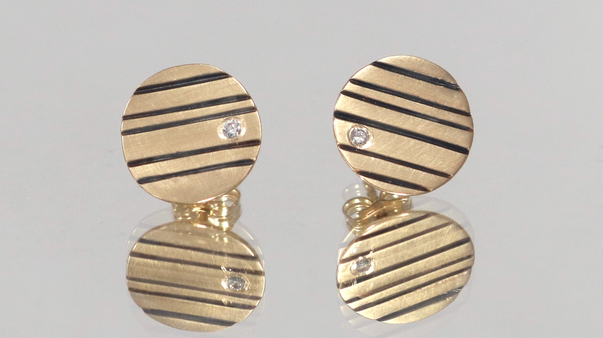 Round 14k gold disc studs with black lines randomly spaced and a single white diamond flush set at the edge.
