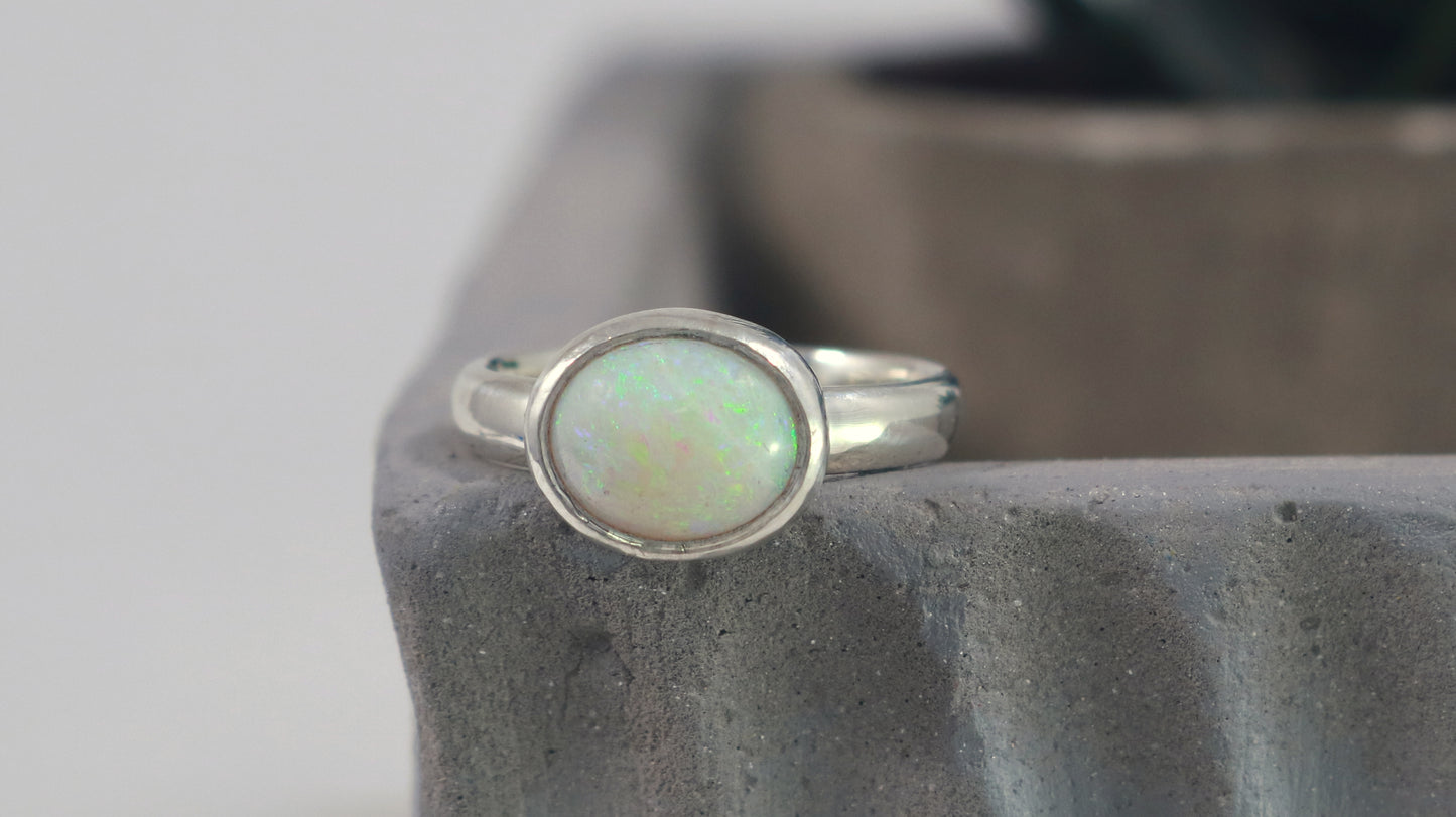 Oval natural white opal set in sterling silver bezel on a sterling silver ring band.