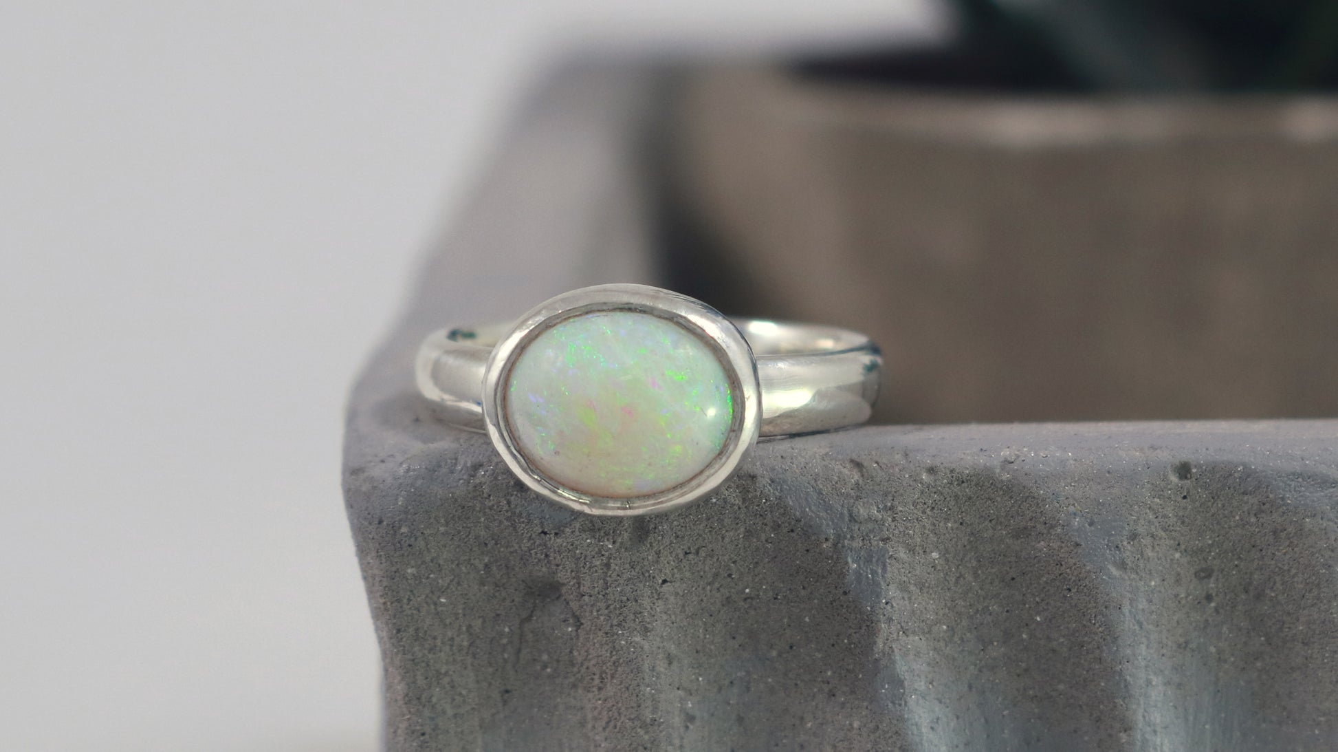 Oval natural white opal set in sterling silver bezel on a sterling silver ring band.