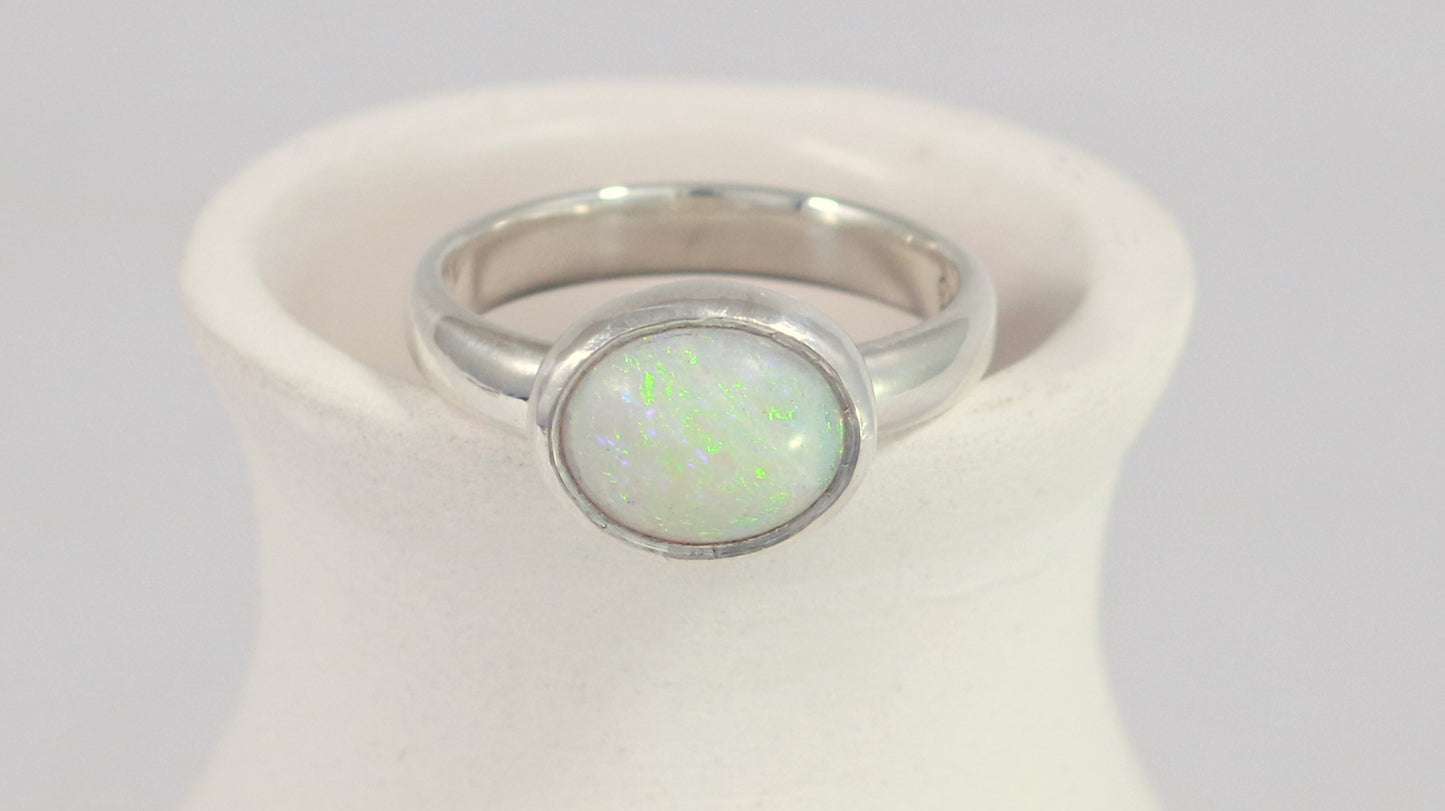 Oval natural white opal set in sterling silver bezel on a sterling silver ring band.
