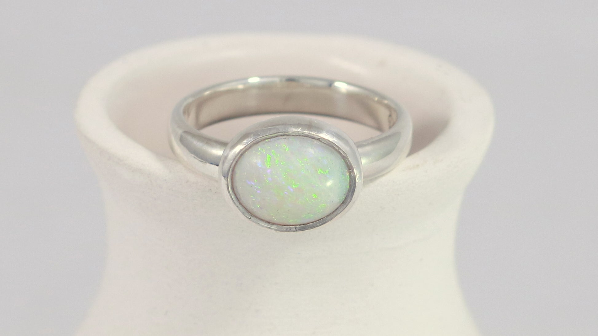 Oval natural white opal set in sterling silver bezel on a sterling silver ring band.