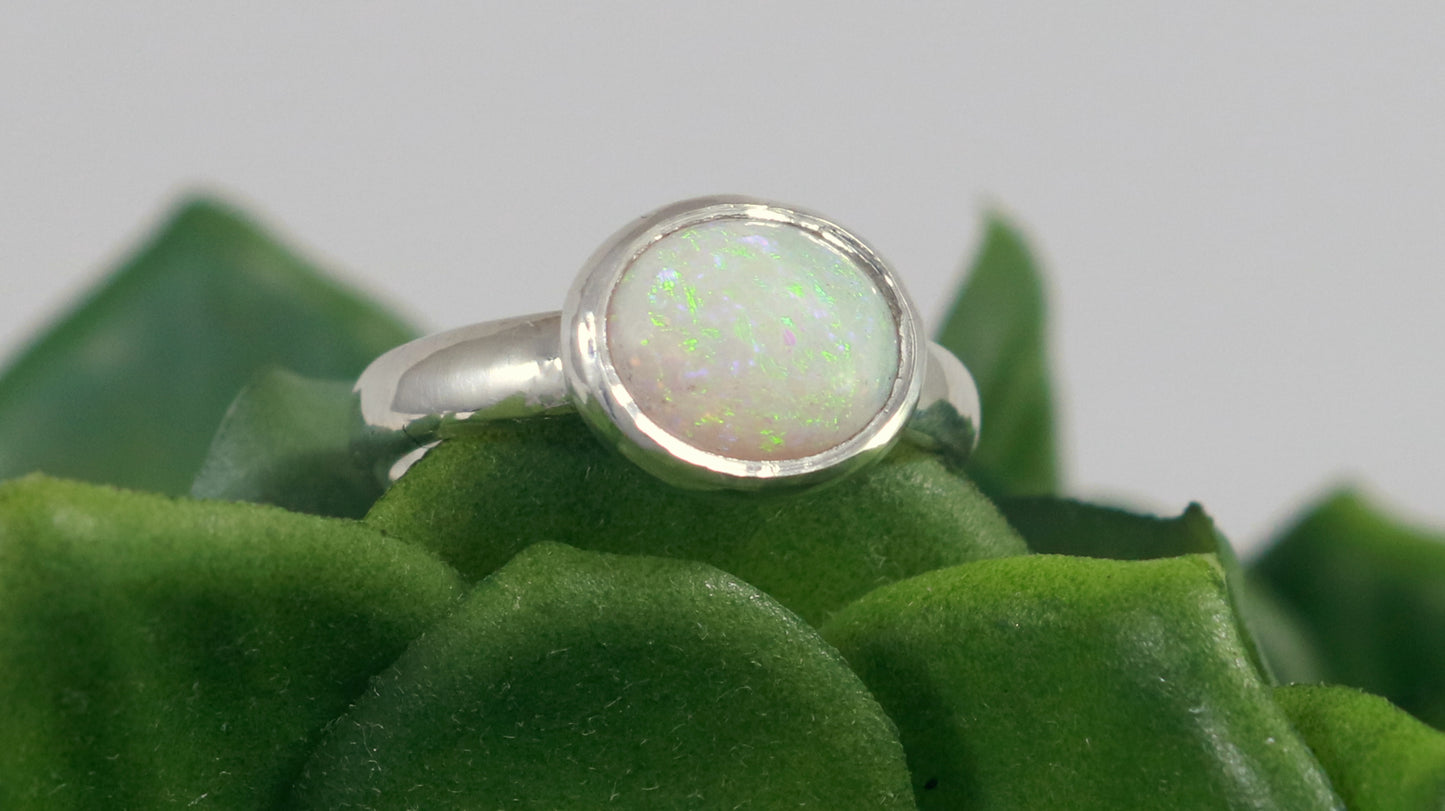 Oval natural white opal set in sterling silver bezel on a sterling silver ring band.