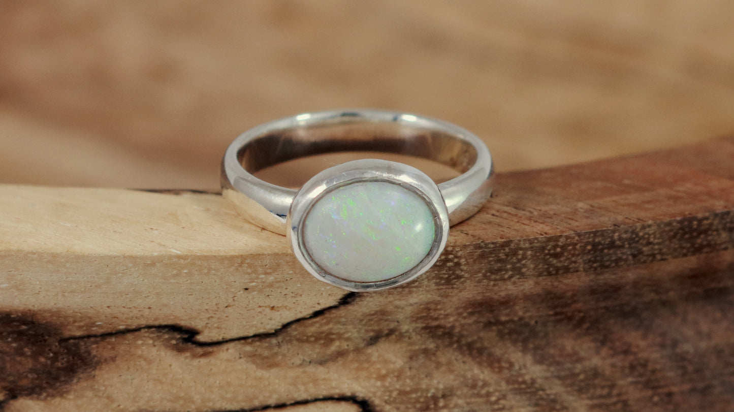 Oval natural white opal set in sterling silver bezel on a sterling silver ring band.
