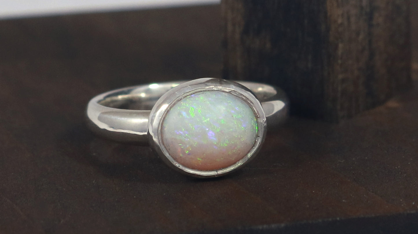 Oval natural white opal set in sterling silver bezel on a sterling silver ring band.