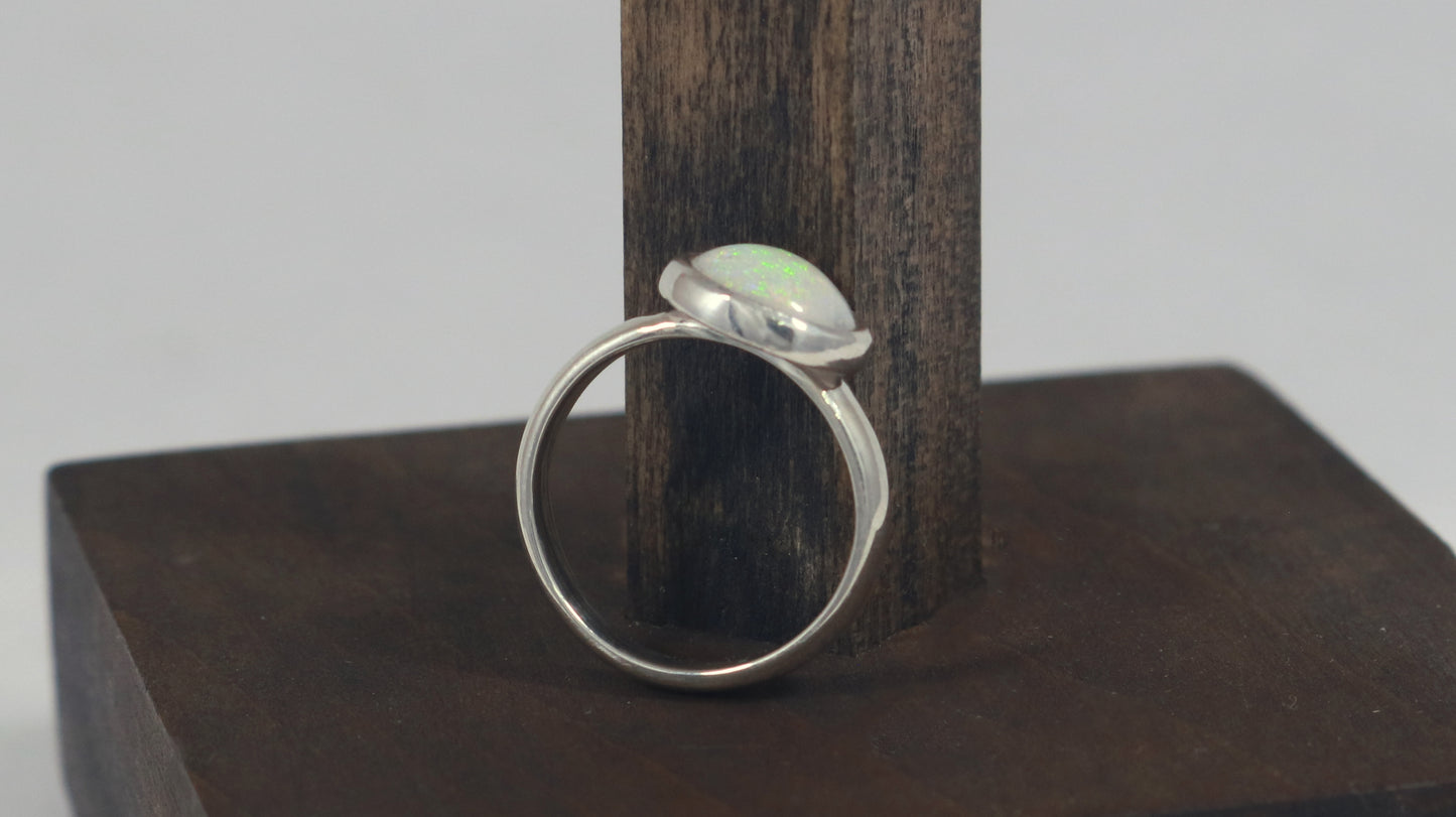 Oval natural white opal set in sterling silver bezel on a sterling silver ring band.