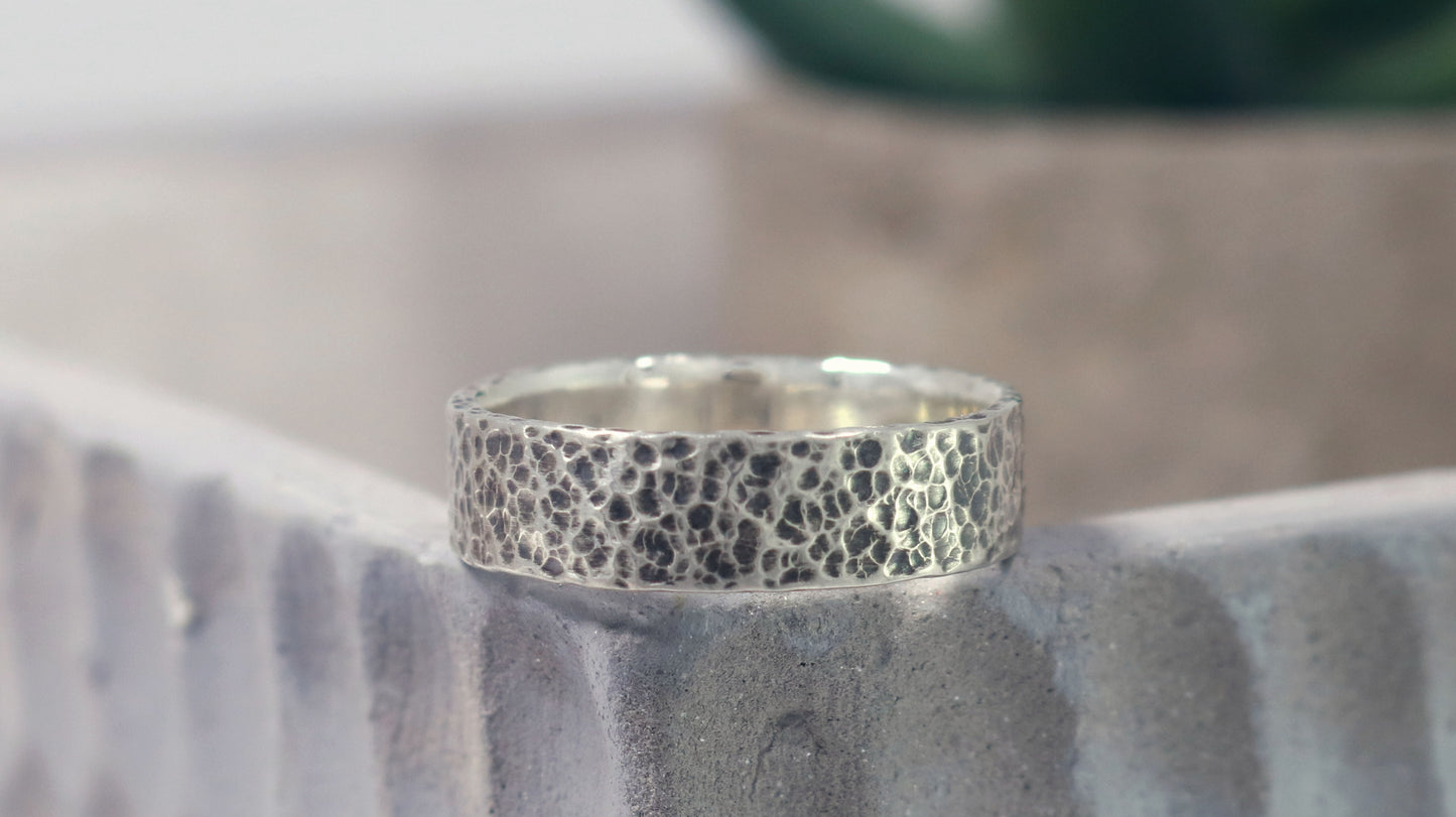 A darkened solid sterling silver ring band, 6mm wide, with small dimpled hammer texture.