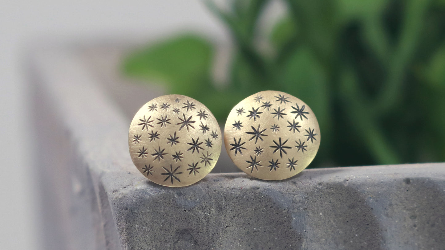 A pair of 14k yellow gold earrings that are 2 domed circles adorned with hand carved black stars.