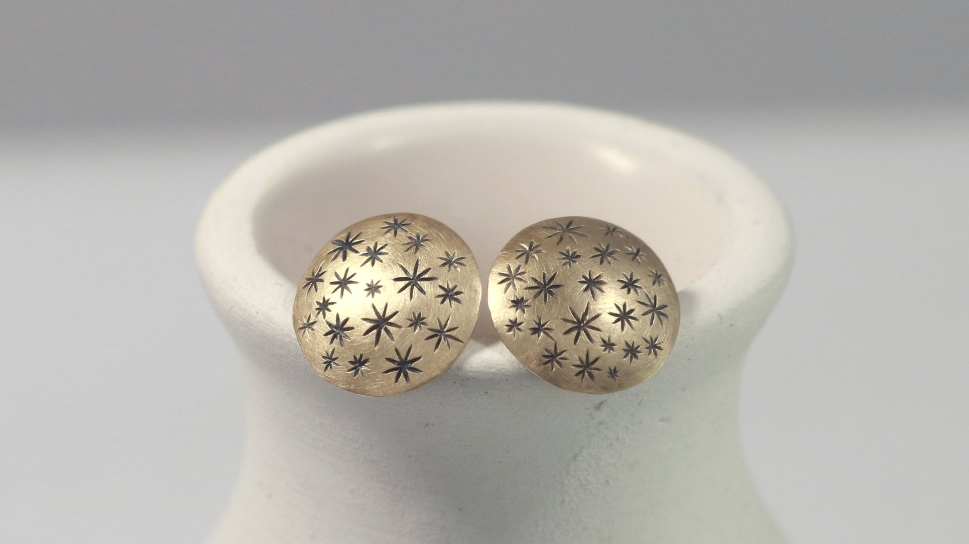 A pair of 14k yellow gold earrings that are 2 domed circles adorned with hand carved black stars.