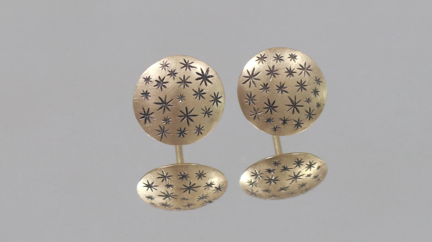 A pair of 14k yellow gold earrings that are 2 domed circles adorned with hand carved black stars.