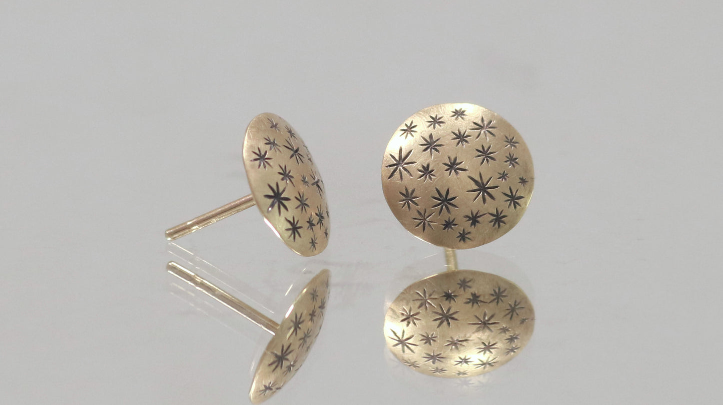 A pair of 14k yellow gold earrings that are 2 domed circles adorned with hand carved black stars.
