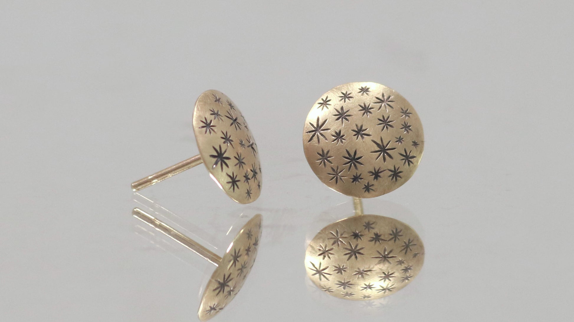 A pair of 14k yellow gold earrings that are 2 domed circles adorned with hand carved black stars.