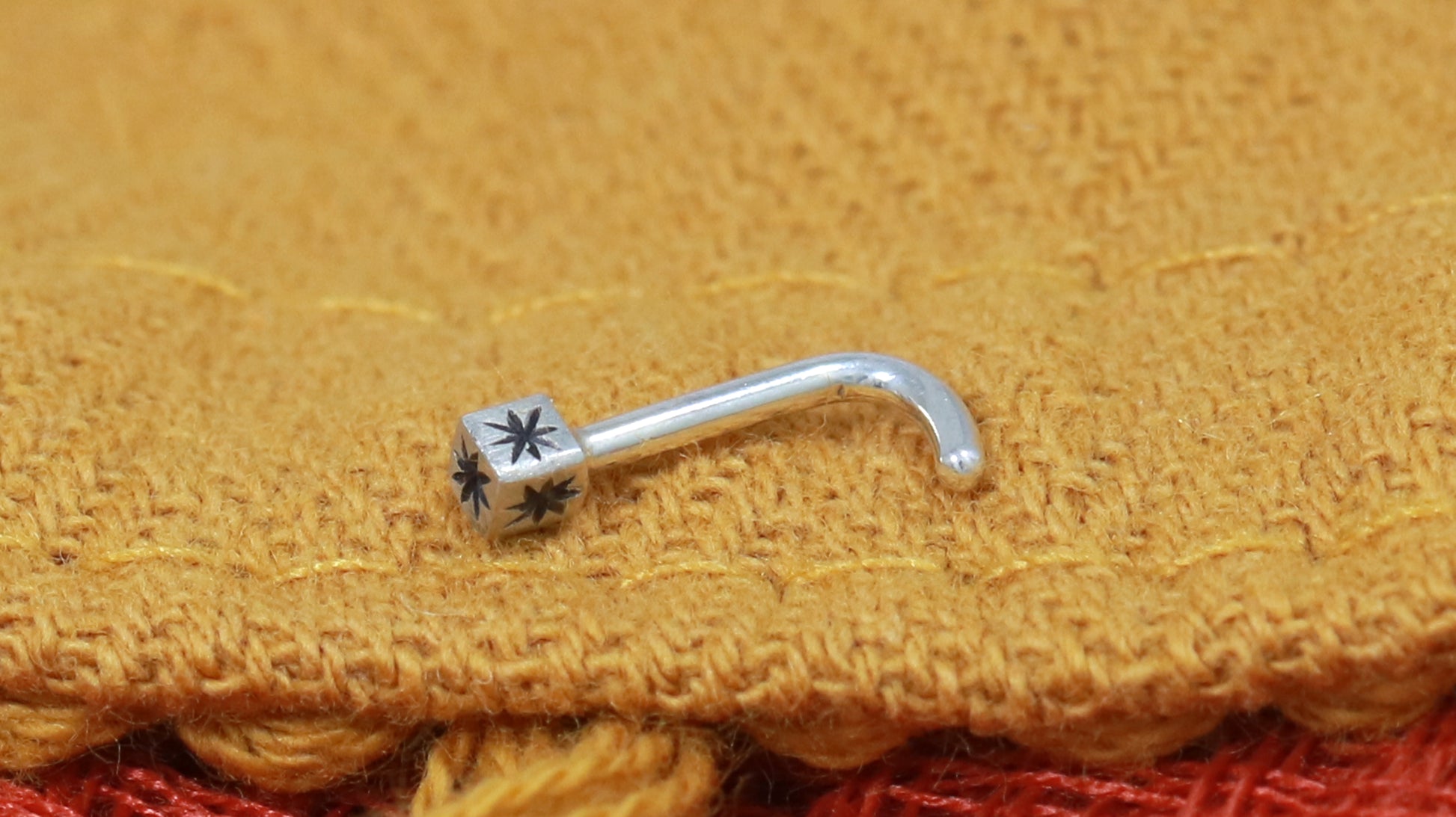 A solid sterling silver cube on a 18g L post nose ring with a hand carved black star on each side.