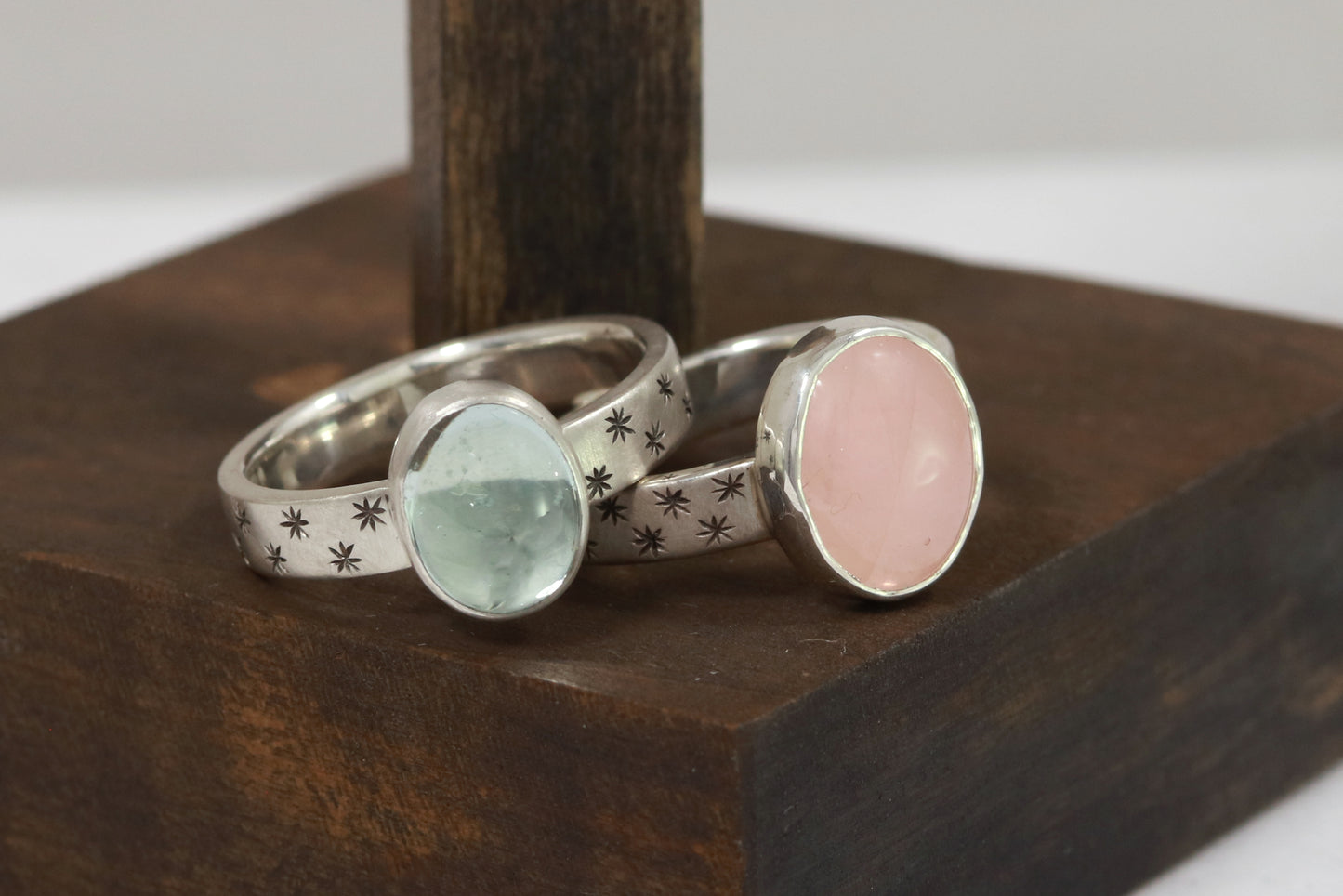 Oval natural gemstone set in sterling silver bezel on a wide sterling silver ring band with checker board of hand cut black stars on either side.