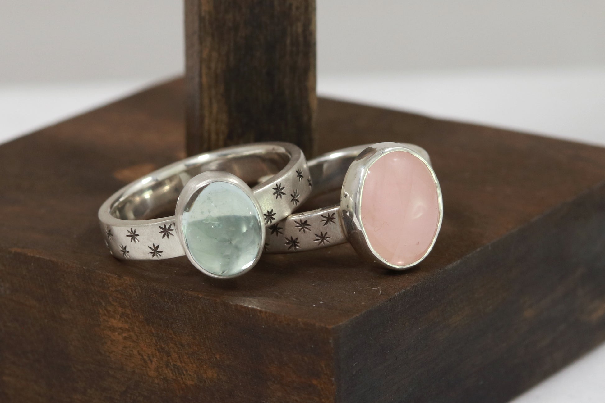 Oval natural gemstone set in sterling silver bezel on a wide sterling silver ring band with checker board of hand cut black stars on either side.