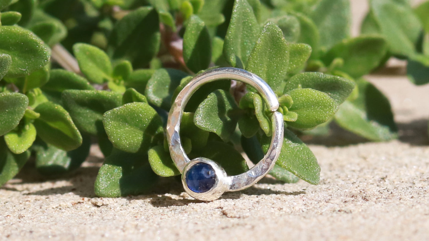 A sterling silver hoop, flattened and textured at the bottom, with a blue sapphire set in a bezel on top of the textured flat section.