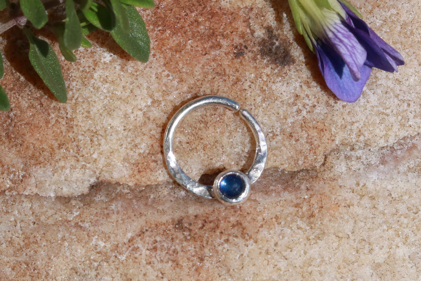 A sterling silver hoop, flattened and textured at the bottom, with a blue sapphire set in a bezel on top of the textured flat section.