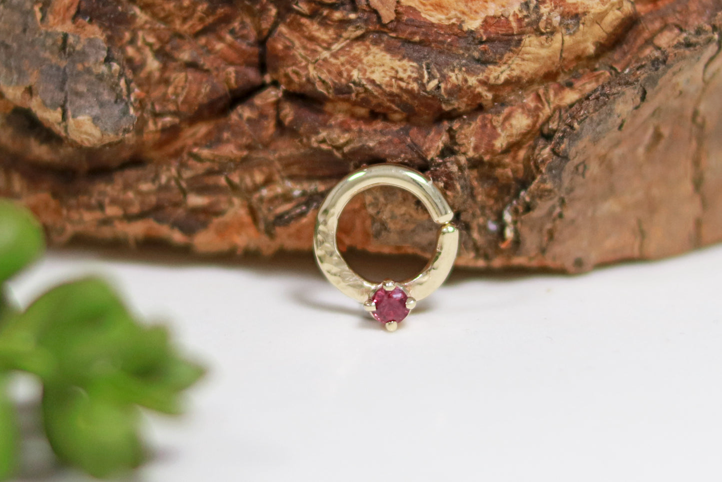 A 14k yellow gold hoop, flattened and textured at the bottom, with a round ruby set with prongs on top of the textured flat section.