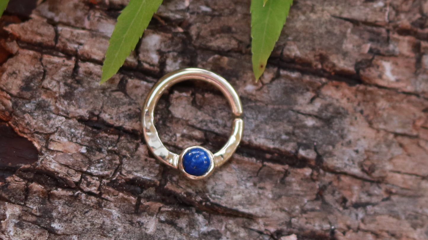 A 14k yellow gold hoop, flattened and textured at the bottom, with a round lapis lazuli set in a bezel on top of the textured flat section.