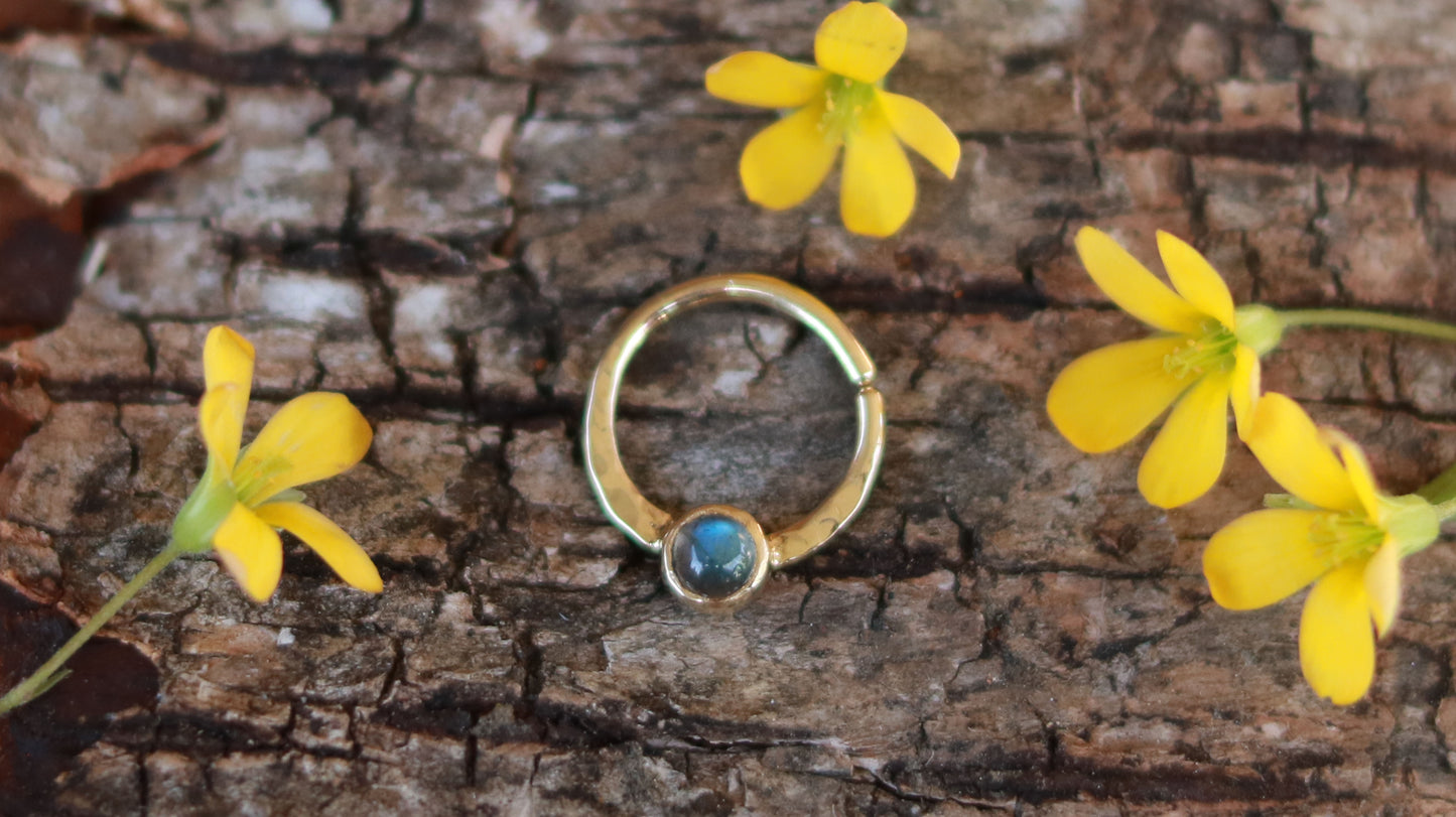 A 14k yellow gold hoop, flattened and textured at the bottom, with a round labradorite set in a bezel on top of the textured flat section.