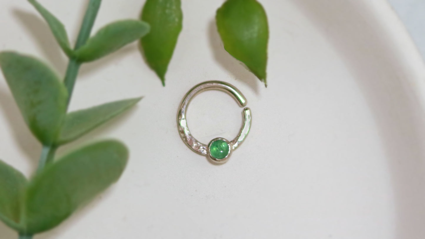 A 14k white gold hoop, flattened and textured at the bottom, with a round emerald set in a bezel on top of the textured flat section.